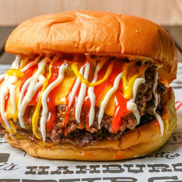 A double cheeseburger with melted cheese, ketchup, mustard, and mayonnaise on a branded paper.