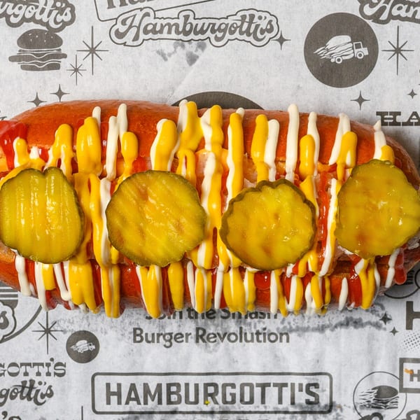 A Hamburgotti's hot dog with mustard, mayonnaise, ketchup, and pickles on branded paper.