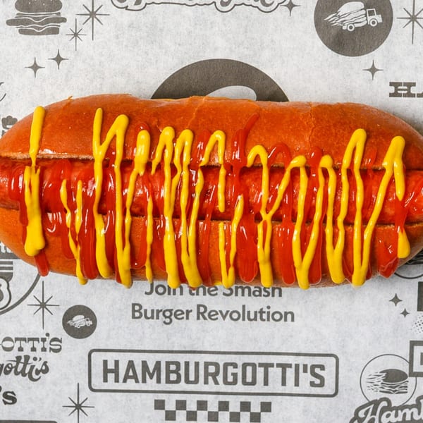 A Hamburgotti's hot dog with ketchup and mustard on branded paper from above.