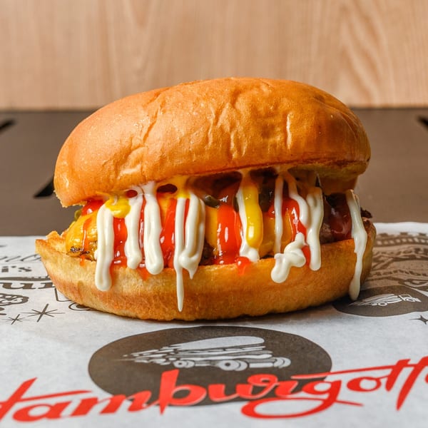 A HamburGotti's burger with ketchup, mustard, and mayonnaise on branded paper.