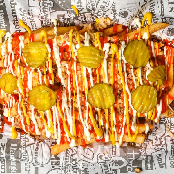 Loaded fries with ketchup, mayonnaise, mustard, and pickle slices in a red basket.